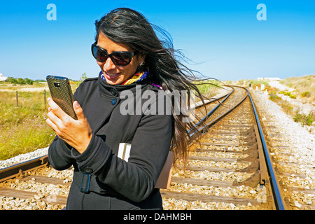 Junge schöne Frau schreibt eine SMS-Nachricht auf ein Bahngleis Stockfoto
