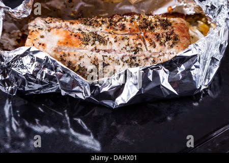 gebackenes Schweinefleisch mit Gewürzen in Alufolie auf schwarzen Tablett Stockfoto