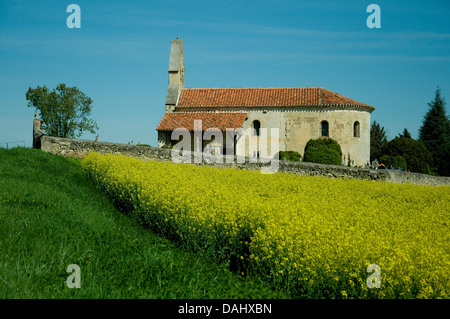 Eine kleine Landkirche im Südwesten Frankreich sich im Frühjahr durch ein Feld von hellen gelben Raps Blumen schmückt - Raps Stockfoto