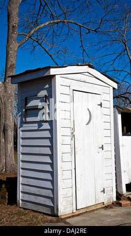 Historisches weißes Nebengebäude mit einem Viertelmond vor der Tür in New Jersey, USA, US-Vintage-out-House-Toilette weiße Eingangstür Bild PT retro Farm Humor Stockfoto