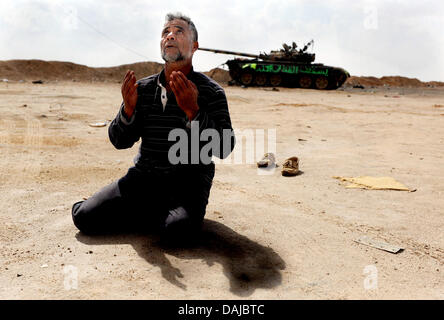 Die libyschen Aufständischen Muftah El Shahomi betet vor ein zerstörter Panzer in Ajdabiya, Libyen. Muammar Al-Gaddafi hat ein Rebell vorgeschlagenen Waffenstillstand abgelehnt. Foto: MAURIZIO GAMBARINI Stockfoto