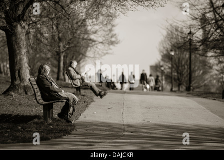 Menschen entspannen auf Parkbänken auf Primrose Hill, London Stockfoto