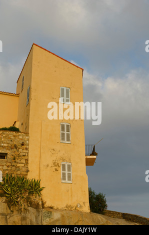 Die Fassade des ein gelbes Haus mit Fenstern und einem Balkon in der Zitadelle von Calvi unter einem bewölkten Himmel. Calvi ist in der Abteilung Stockfoto