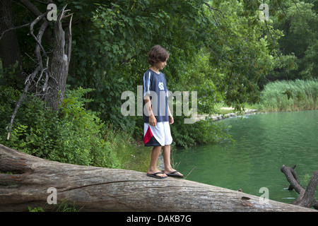 Junge geht vorsichtig auf einen großen Baumstamm, der ins Wasser auf dem See am Prospect Park, Brooklyn, NY fiel. Stockfoto