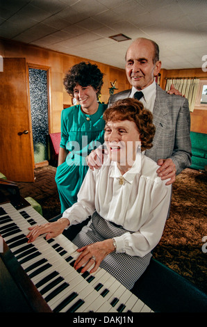 Ein reifer Mann und Frau sind durch ihre erwachsene Tochter in ein Singalong an der Familie Orgel zu Hause in Riverside, Kalifornien verbunden. Stockfoto