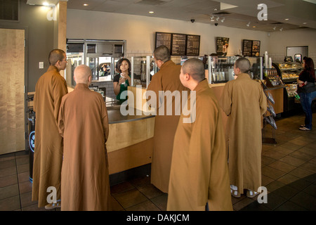 Kontrast zu ihrer Umgebung, kaufen drei buddhistische Mönche und eine Nonne in braunen Roben und rasierten Köpfen, Getränke in Starbucks. Stockfoto