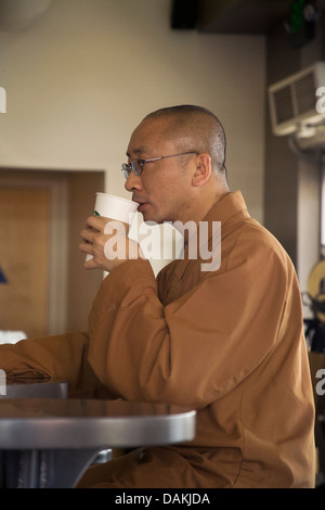 Kontrast zu der Umgebung, ein asiatischer buddhistischer Mönch in braunen Roben und rasierten Kopf, aktualisiert sich selbst in einem Starbucks-Café. Stockfoto