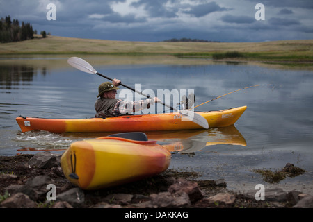 Junger Mann in gelb orange Kajak ist in einen See in Arizona mit seinen Füßen und Angelrute aufgestützt auf der Vorderseite des Boot paddeln. Stockfoto