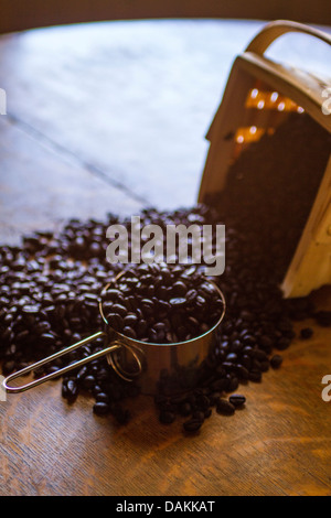 Kaffee Bohnen verschütten aus einem Birkenholz-Korb auf einem antiken Eichentisch Stockfoto