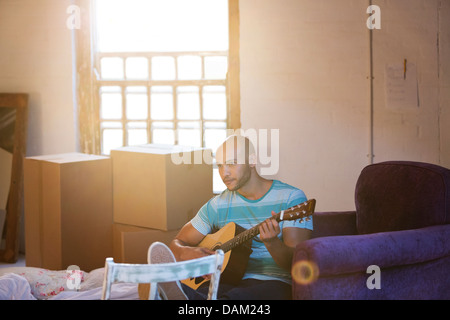 Mann spielt Gitarre im neuen Zuhause Stockfoto