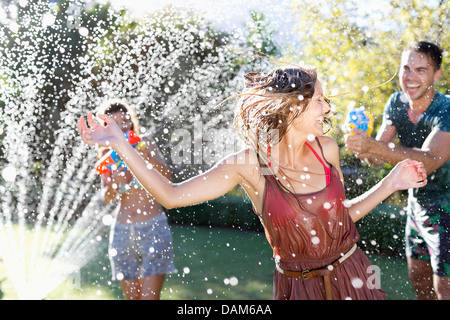 Freunde spielen mit Wasserpistolen in sprinkler Stockfoto