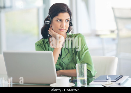 Geschäftsfrau mit Kopfhörern am Schreibtisch Stockfoto