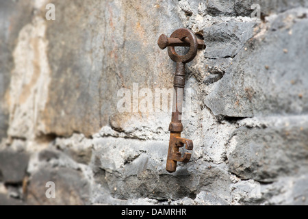 Alte rostige Schlüssel hängen an einem rostigen Nagel in einer Steinmauer Stockfoto