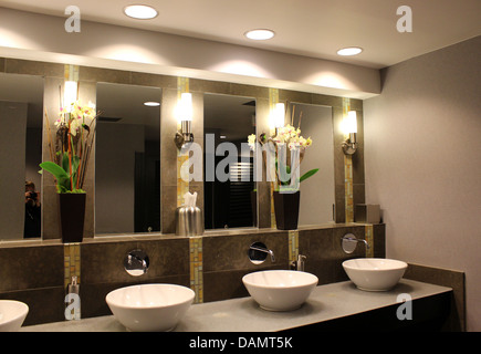 Ultra schickes Badezimmer mit ausgefallenen Waschbecken, Spiegel und Blumenarrangements, dezente Beleuchtung Verwaltungsaufwand für gehobenes Stadthotel. Stockfoto