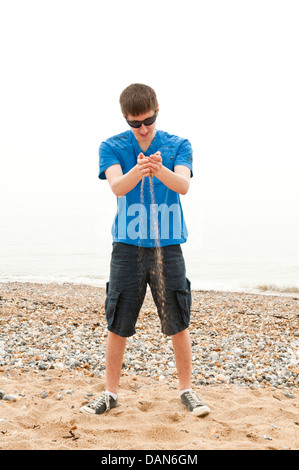 Ein junger Mann stehend an einem Strand und Sand durch die Finger laufen zu lassen Stockfoto