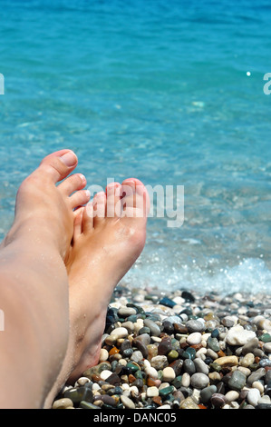 junge weibliche Füße am Strand mit blauem Wasser Stockfoto