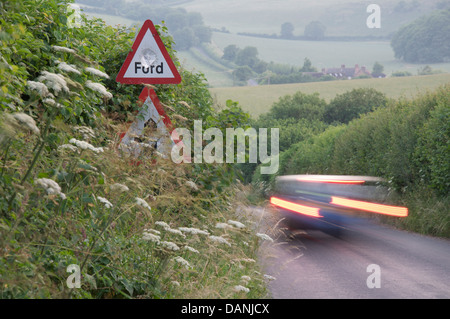 Englische Landschaft. Die roten Rückleuchten eines Auto-Streifen durch die grüne Hecken einen schmalen Feldweg in Dorset. Ein Schild warnt vor einer Furt. Stockfoto