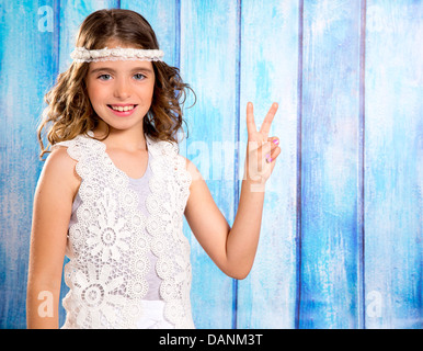 Brünette glückliche Kinder Hippiemädchen lächelnd mit Hand Friedenszeichen auf blau Holz Stockfoto