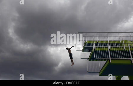 Ein Junge springt von einem Sprungturm in einem Freibad in Nürnberg, während dunkle Gewitterwolken am Himmel, Deutschland, 10. August 2011 ergeben. Niedrige Temperaturen und Regen verursacht haben Rückgänge im Vertrieb für Freibäder und Biergärten. Foto: Daniel Karmann Stockfoto