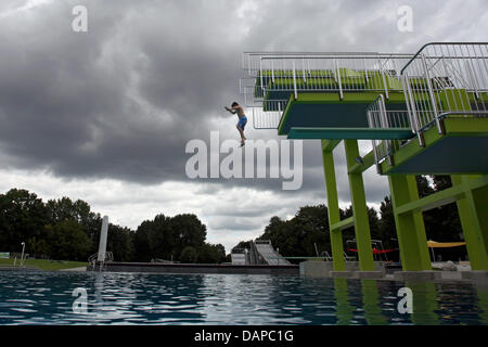 Ein Junge springt von einem Sprungturm in einem Freibad in Nürnberg, während dunkle Gewitterwolken am Himmel, Deutschland, 10. August 2011 ergeben. Niedrige Temperaturen und Regen verursacht haben Rückgänge im Vertrieb für Freibäder und Biergärten. Foto: Daniel Karmann Stockfoto