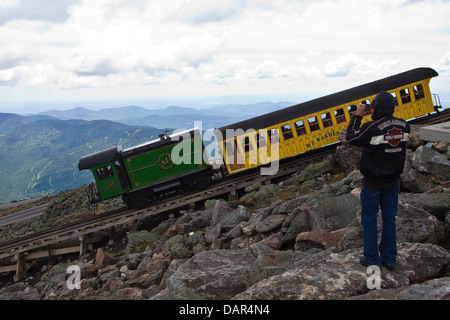 Ein Mann fotografiert die Mount Washington Cog Railway mit seinem Handy, als der Zug den Gipfel des Berges in New Hampshire verlässt Stockfoto