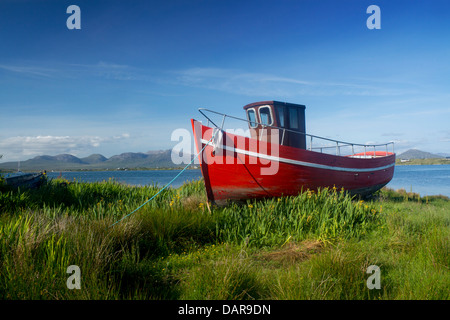 Roten Fischerboot am Ufer der Mündung Roundstone Connemara einige der zwölf Pins / Twelve Bens im Hintergrund Co Galway Irland Stockfoto