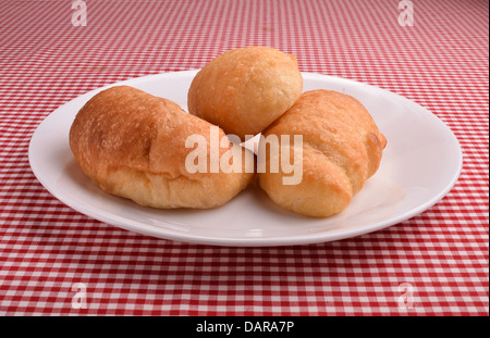 Drei Croissants legen auf einem weißen Teller auf einem roten und weißen Check Tuch. Stockfoto