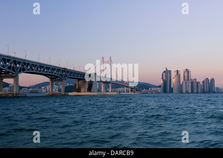 Wohngebäude und Hotels in Haeundae, Busan, Südkorea und Gwangan-Brücke in der Dämmerung, aus dem Meer gesehen. Stockfoto
