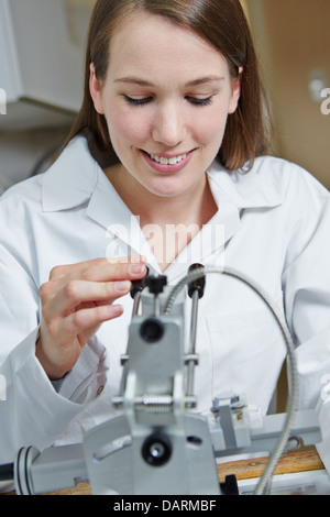 Junge Frau am Bohrmaschine für randlose Brille in Ausbildung bei Optiker Stockfoto