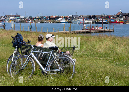 Ein paar Radfahrer machen Sie eine Pause auf einer Bank mit Blick auf die Mündung bei Blackshore in der Nähe von Walberswick in Suffolk - England. Stockfoto