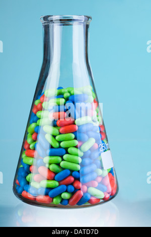 Kolben mit grünen, blauen und roten Tabletten und Pillen auf blau Stockfoto