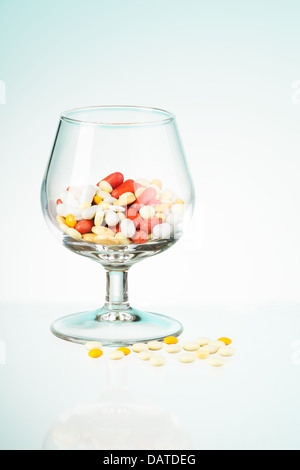 Problemstellung, dargestellt von Whisky-Klasse voll von verschiedenen Medikamenten und Pillen, die verstreut auf den Tisch zu trinken Stockfoto