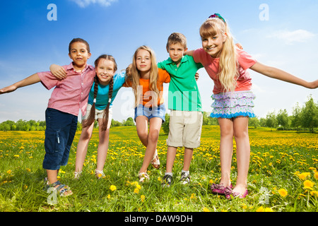 Fünf glückliche Kinder umarmen zusammen stehen im Feld Löwenzahn Stockfoto