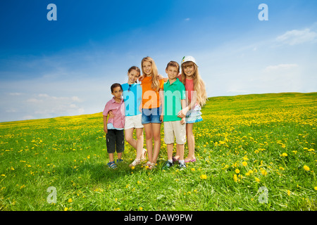 Fünf glückliche Vielfalt aussehende Kinder Freunde stehen in der Blumenwiese Stockfoto