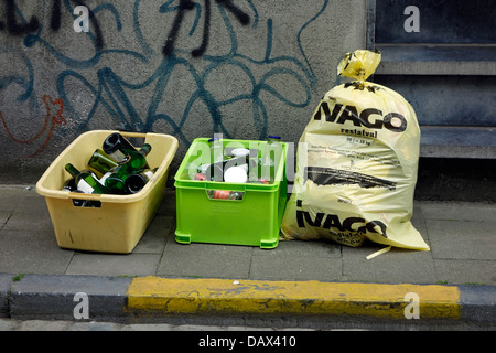 Kunststoff-Behälter mit Glas-Flaschen und Müll-Tasche mit Hausmüll vor Haus in Stadtstraße Stockfoto