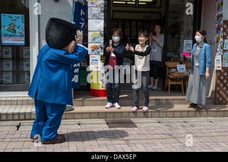 Japanische Touristen nehmen Fotos von Shigeru Mizuki Salaryman Yamada Charakter im Kostüm unterwegs Kitaro in Sakaiminato, Japan Stockfoto