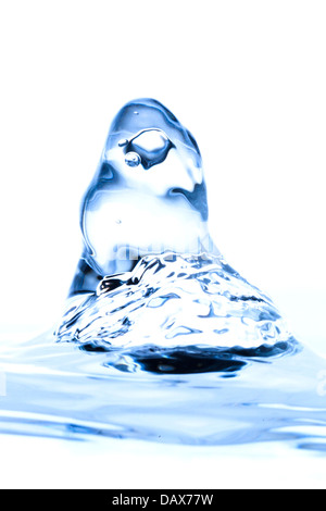 Eine Nahaufnahme eines Wasserspritzers nahm die mittlere Bewegung auf und bildete eine kronenartige Struktur mit sichtbaren Luftblasen, die im durchsichtigen blauen Wasser eingeschlossen sind. Der Spritzer steigt von einer ruhigen Wasseroberfläche auf Stockfoto