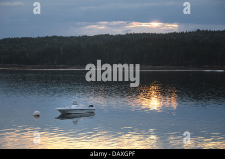 Ein kleines Motorboot vertäut off Shore mit reflektierenden Sonnenuntergang im Wasser Stockfoto