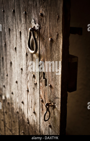 Alte Holztür links angelehnt. Holzbohle Bau mit Metall-Nieten, Griff und Haken. Stockfoto
