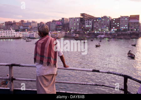 Ein Mann wacht startet und Fähren, die Passagiere von und nach Sadarghat am Fluss Buriganga in Dhaka, Bangladesch in der Abenddämmerung Stockfoto