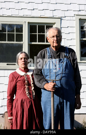 Frau und Mann stellte vor einem weißen Bauernhaus mit einer Heugabel, wie die Malerei Stockfoto