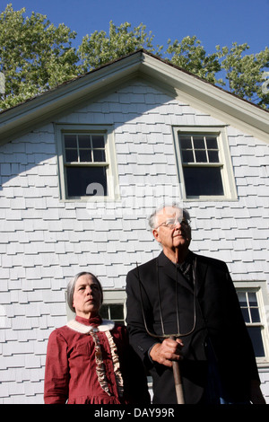 Frau und Mann stellte vor einem weißen Bauernhaus mit einer Heugabel, wie die Malerei Stockfoto