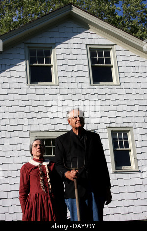 Frau und Mann stellte vor einem weißen Bauernhaus mit einer Heugabel, wie die Malerei Stockfoto