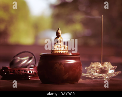 Kleine Statue des Meditierenden Buddha, Rauchen, Räucherstäbchen und buddhistischen Tingsha Glockenspiel Glocken künstlerischen Stillleben Stockfoto