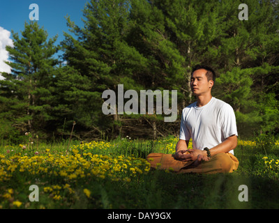 Lizenz verfügbar unter MaximImages.com - Shaolin-Meister meditiert im Freien während Sonnenaufgang in der Natur, sitzt mit gekreuzten Beinen Stockfoto