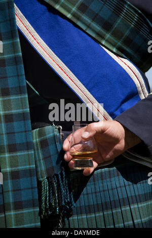 Tomintoul, Schottland, Großbritannien. 20. Juli, 2013. Herr Bill Barclay, 57 das Tragen der gedämpften Tartan Schärpe, und Feiern mit einem Glas nip der schottischen Whisky, Montieth bei der jährlichen Tomintoul Highland Games und sammeln am 3. Samstag im Juli statt. Dieses sportliche, historische und traditionelle Veranstaltung ist auf dem Showground im Dorf statt. Stockfoto