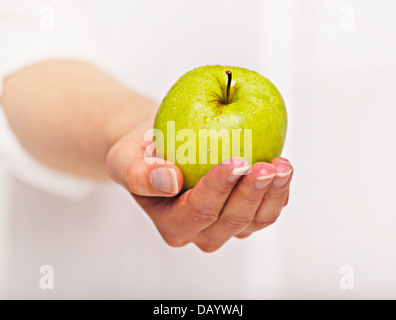 Zarte Frauenhand geben einen grünen Apfel Stockfoto