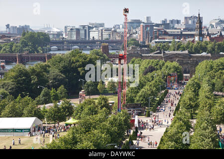 Glasgow, Schottland, 21. Juli 2013. Einen erhöhten Blick der Besucher auf der Glasgow Show 2013 auf Glasgow Green vor dem Hintergrund des Flusses Clyde, Merchant City und der International Financial Services District im Zentrum der Stadt. Einige Zelte in der Landschaft Zone und Festplatz Fahrten können gesehen werden. Stockfoto