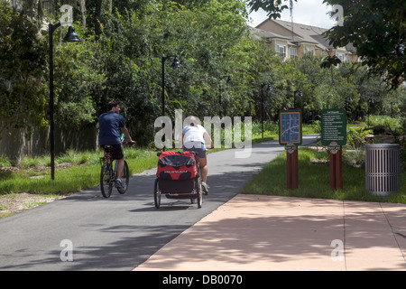 Paar Fahrrad ziehen Anhänger Kinderwagen Schienen Trails Depot Radweg neben dem Campus der University of Florida. Stockfoto