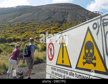 Touristen gehen ein Schild warnt gleichzeitig vor den giftigen Schwefel Fumarolen Flucht vor dem Vulkan Gran Cratere auf der Äolischen Insel Vulcano in Italien, 30. Mai 2007. Die Äolischen Inseln mit den wichtigsten Insel Liparei und Salina sind eine vulkanische Inselgruppe Offshore-Nordküste Sizilien. Die Inseln bestehen aus Asche und Lava von meist erloschenen Vulkanen. Die Zugehörigkeit zu der Provinc archipleago Stockfoto